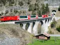 The red and white Glacier Express train travels across a stone viaduct, a scenic journey from Chur to Zermatt.