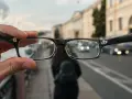 Okulary trzymane przed zamazanym miejskim tłem z samochodami.