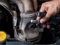 Druga sonda lambda objawy: mechanik trzyma nową sondę lambda przy kolektorze wydechowym.