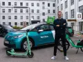 Ein Mann steht stolz neben einem Bolt Drive Auto, E-Scooter und Fahrrad. Er ist ein Bolt Fahrer, der umweltfreundliche Mobilität fördert.