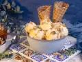Schüssel mit Eiscreme, garniert mit Nüssen und Honig. Ein Glas Honig und Waffelhörnchen im Hintergrund. Ein süßer Genuss: Eis mit Honig statt Zucker.