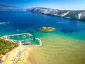 Piaszczyste plaże w Chorwacji, z turkusową wodą, łodziami w marinie i ludźmi cieszącymi się słońcem.