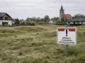 Tablica informuje o stanowiskach archeologicznych. W tle domy i kościół.