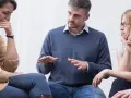 Uomo con aria autoritaria parla a un gruppo, una donna piange. Sembra un collega che vuole comandare.