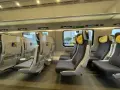 Wnętrze pociągu Pendolino z rzędami szarych foteli z żółtymi zagłówkami.