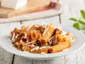 Piatto di pasta alla norma con rigatoni, melanzane fritte, pomodoro e ricotta salata grattugiata.