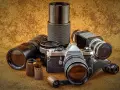 Kolekcja różnych rodzajów aparatów fotograficznych i akcesoriów, w tym aparat Pentax, obiektywy i klisze.