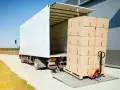 Stos kartonów na palecie, gotowy do załadunku do białej ciężarówki. Ubezpieczenia cargo chronią takie przesyłki.
