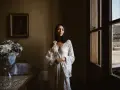 Kobieta w białej sukni, obok bukiet kwiatów. Scena sugeruje przygotowania do ślubu za granicą, co wyjaśnia przyczyny popularności wesel typu "destination wedding".