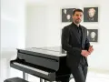 Uomo con elegante outfit per andare a teatro, in completo nero, accanto a un pianoforte a coda.