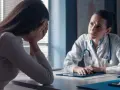 Kobieta w gabinecie lekarskim, ze smutkiem ukrytym w dłoniach, słucha diagnozy. Lekarka z troską pochyla się nad dokumentami, być może omawiając poronienie chybione.