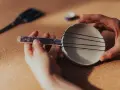 Jak zrobić instrument muzyczny do szkoły? Ręce składają prosty instrument z talerzyka, gumek i patyczka.