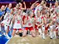 Siatkarki reprezentacji Polski w siatkówce, uśmiechnięte, pozują do zdjęcia, wskazując palcami w górę.