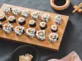 Frisch zubereitetes Sushi-Rezept auf einem Holzbrett, mit Gurke, Karotte und Ei gefüllt. Dazu Sojasauce und eingelegter Ingwer.