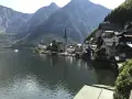Malowniczy widok na Hallstatt, miasteczko nad jeziorem, z górami w tle. Widać kościół i domy, a na wodzie statek. To miejsce słynie z kopalni soli.