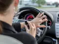 Frau tippt auf ihre Smartwatch am Steuer. Handy am Steuer Strafe vermeiden!