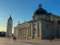 Wileńskie kościoły: Katedra i dzwonnica na placu. Słońce oświetla monumentalną architekturę, tworząc długie cienie.