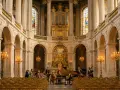 Un orchestre joue dans la chapelle royale de Versailles, devant un orgue doré et des vitraux.
