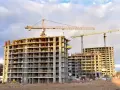 Budowa wielopiętrowych budynków mieszkalnych z żurawiami budowlanymi w tle.