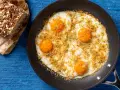 Uova fritte in padella, condite con pangrattato e erbe aromatiche, perfette per le tue ricette con uova. Accanto, una fetta di pane integrale.