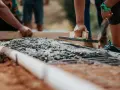 Pracownicy wyrównują świeży beton na fundamencie. Jaki beton na fundament b20 czy b25?