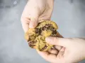 Hände halten einen frisch gebackenen American Cookie mit geschmolzener Schokolade. Perfekt zum amerikanischen Cookies backen!
