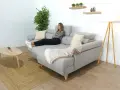 Mujer relajada en un sofá en medio del salón, con una manta y cojines.