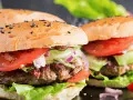 Dwa soczyste burgery wołowe z bułką, pomidorem, sałatą i ogórkiem.