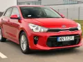 Czerwony Kia Rio w ruchu. Kierowca w okularach za kierownicą. Wiele pozytywnych kia rio opinie o tym modelu.