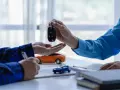 Przekazanie kluczyków do auta w ramach leasingu dla firm. Na stole modele samochodów i dokumenty.