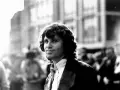 Jim Morrison, mit seinem charakteristischen lockigen Haar und einem nachdenklichen Blick, steht im Gegenlicht.