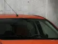 Pomarańczowy samochód z przyciemnianymi szybami z przodu, z antenką na dachu, stoi przy betonowej ścianie.