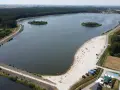 Opolskie atrakcje: piaszczysta plaża nad jeziorem, wyspy, las i mostek. Ludzie odpoczywają i kąpią się.