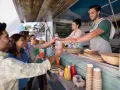 Uśmiechnięci ludzie odbierają napoje od barmanów z food trucka.