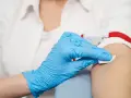 Ręka w niebieskiej rękawiczce dezynfekuje skórę przed pobraniem krwi.