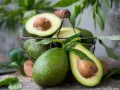 Des avocats frais, entiers et coupés en deux, dans un panier. Pour savoir comment avoir un avocatier qui donne des fruits, il faut de la patience et de bons soins.