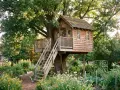Ein wunderschönes Baumhaus, das zum baumhaus selber bauen inspiriert. Umgeben von einem blühenden Garten und alten Bäumen.