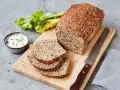 Ein rustikales Chia Brot, frisch aufgeschnitten, mit Sellerie und Dip auf einem Holzbrett.