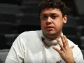 Mężczyzna z kręconymi włosami, Jakub Skrzywanek, w białym golfie gestykuluje podczas rozmowy.