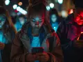 Młodzi ludzie pogrążeni w ekranach telefonów, zmagający się z nomofobią w nocnym mieście.