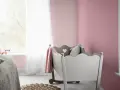 Pokój dziecięcy z łóżeczkiem, pluszowym królikiem i kocem w kolorze amarant. Ściany pomalowane na delikatny róż.