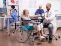 Rehabilitacja po uszkodzeniu móżdżku: pacjentka w wózku wykonuje ćwiczenia z hantlami pod okiem fizjoterapeuty.