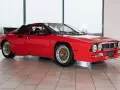 Czerwona Lancia 037 z czarnym spojlerem i złotymi felgami, gotowa do rajdu.
