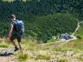Turysta z plecakiem schodzi po kamienistej ścieżce w Karkonoszach. W dole widoczny schronisko, jedna z wielu atrakcji górskich.