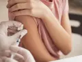 Osoba w białej rękawiczce podaje zastrzyk w ramię.