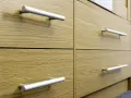 Poignées de tiroirs en aluminium sur des meubles en bois clair. Un guide visuel pour comment fixer un bouton de meuble.