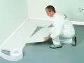 Mężczyzna w białym kombinezonie układa styropian na podłodze.