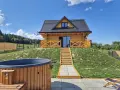 Uroczy domek na odludziu z drewnianą werandą i schodami prowadzącymi do drzwi. Przed domkiem jacuzzi i leżaki.