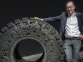 Wim Delvoye pose à côté d'une roue ornée de dragons, une œuvre d'art monumentale.