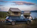 Två bilar med takboxar som fungerar som tält står redo för camping vid en sjö. En eld sprakar i förgrunden. En perfekt plats för camping i Gnesta.